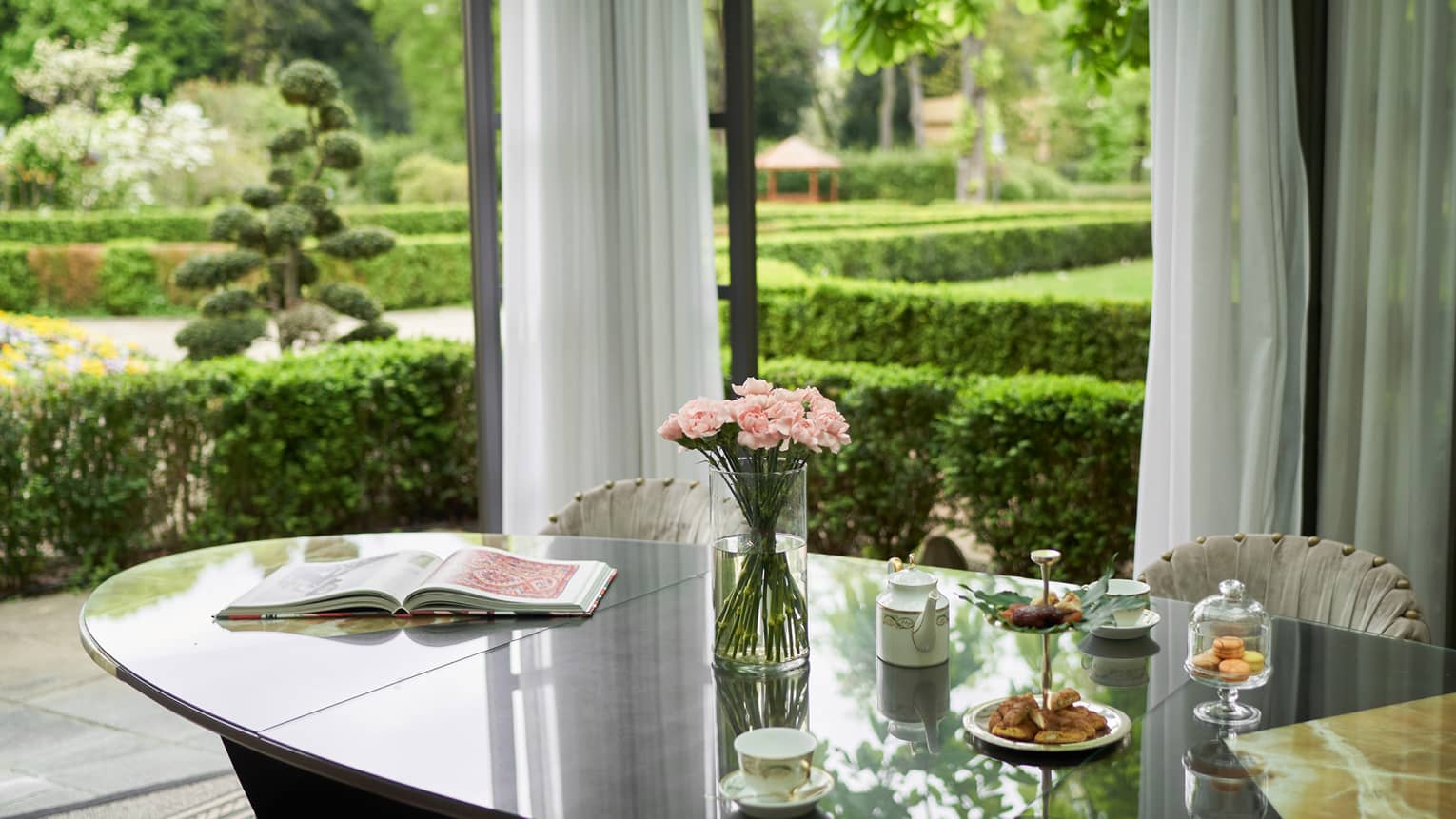 Oval dining table set with afternoon tea and flowers, garden in the background