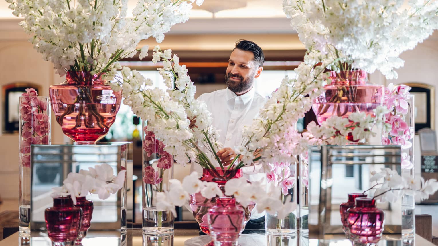Floral designer standing behind large display of white flower sprays in assorted pink vases
