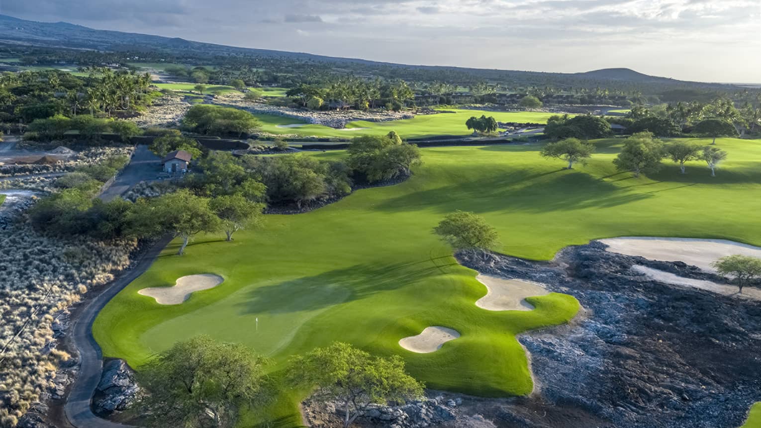 An overhead view of a lush green golf course under a cloudy sky.