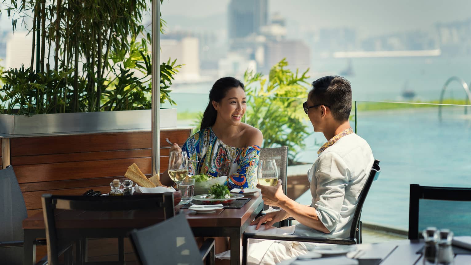 Two people smiling, dining at sunny Poolside Terrace patio table