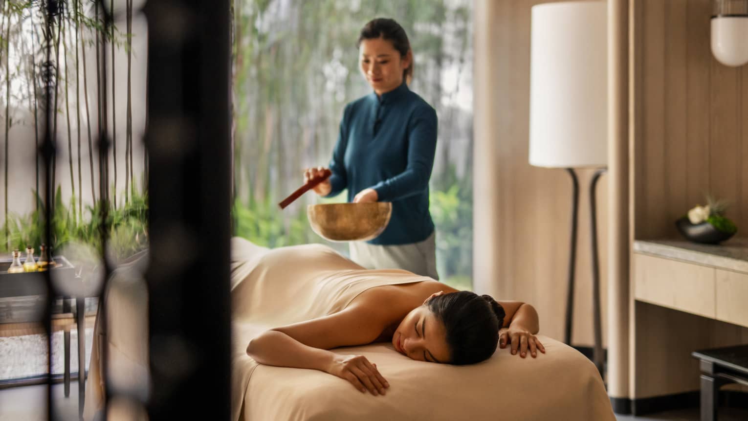 Female spa therapist performs singing bowl spa ritual for woman on spa treatment table and luxury hotel spa