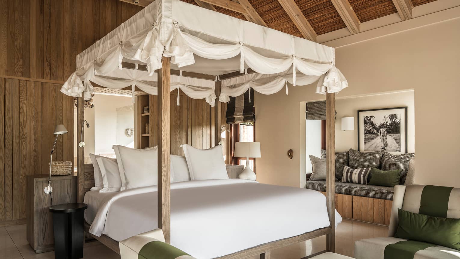 White canopy with ties at top of poster bed, behind sofas and cushioned bench
