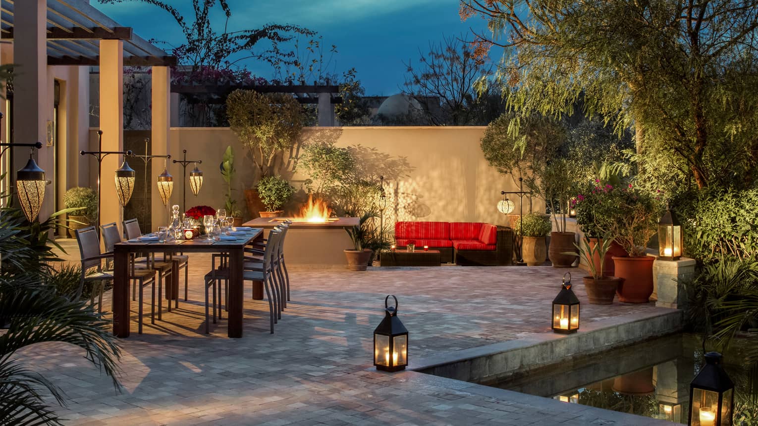 Two-bedroom villa patio with long candle-lit private dining table, outdoor fireplace, lanterns along pool