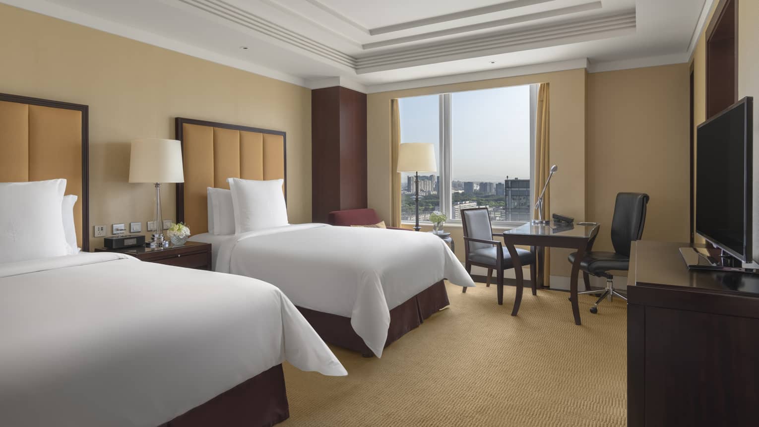 Hotel room with two single beds, tan headboards, tan carpet, desk and window