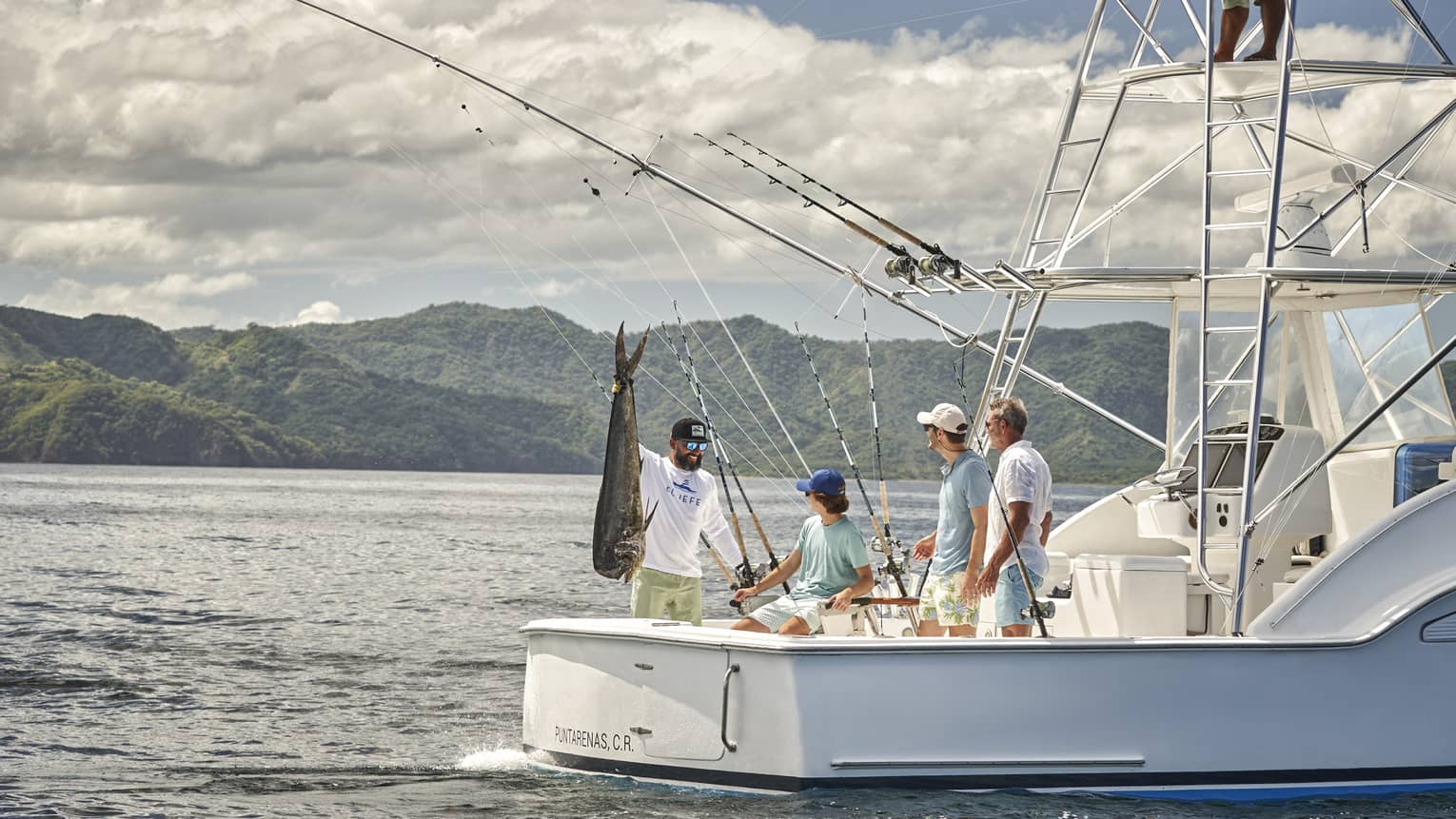 Four men are gathered on the back of a fishing boat with one of them holding a large fish up by the tail
