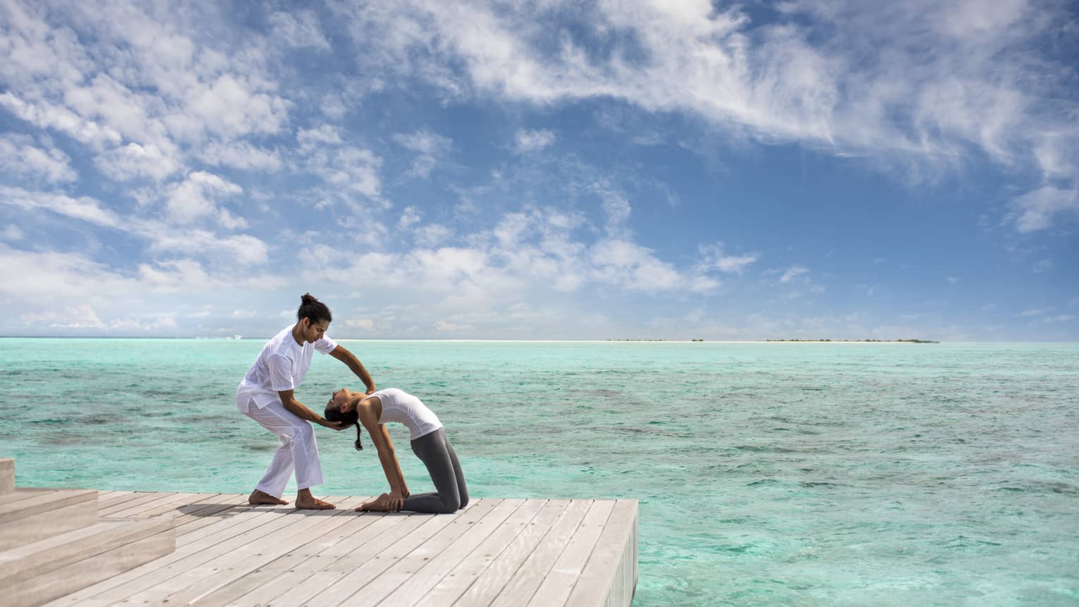 Woman leans back into hands of Yoga Therapist on dock over lagoon