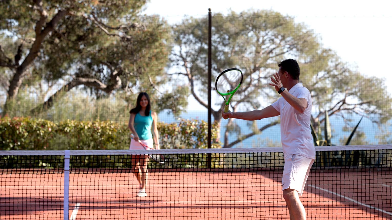 Man swing tennis racket, woman on other side of net