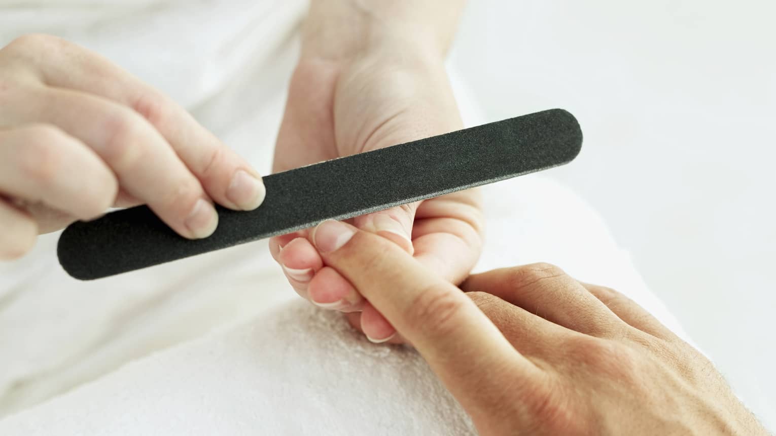 Woman holds manicure nail file to man's fingernails over white towel