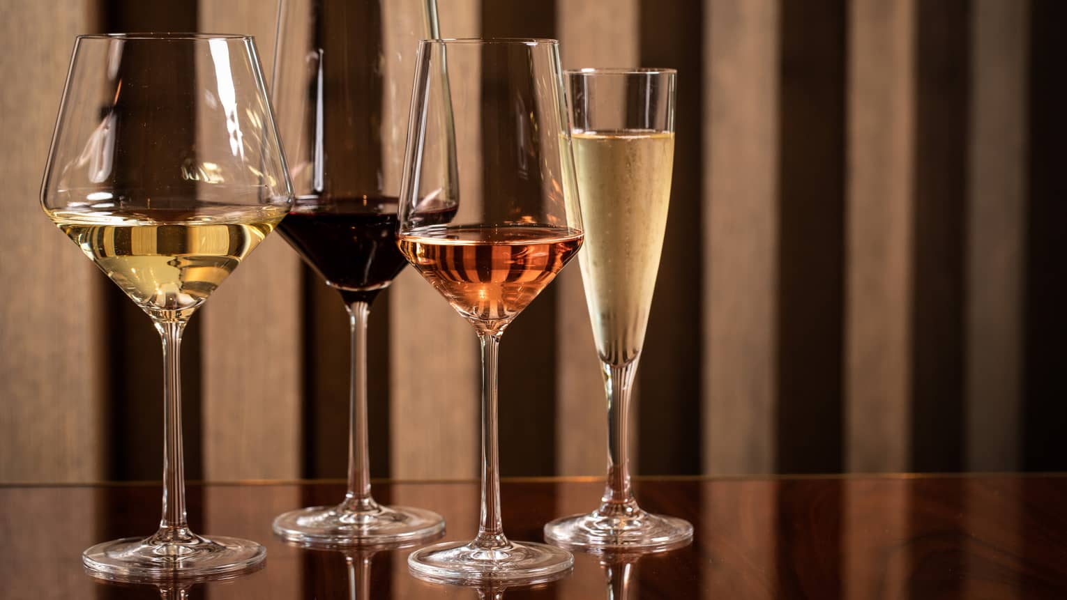 Four modern wine glasses holding white, red and rose wine are lined up on a wooden table