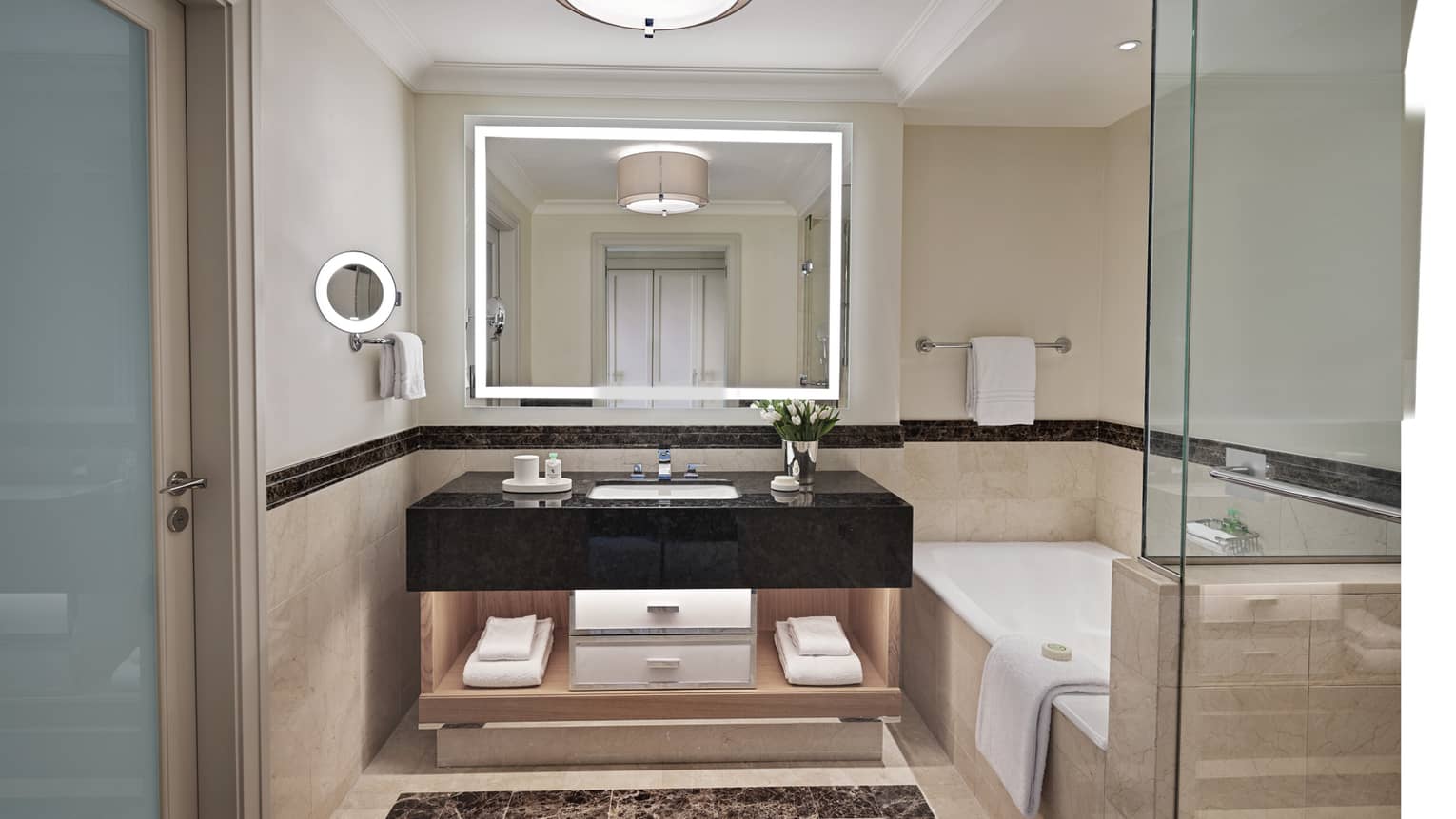 Bathroom with lighted mirror, black marble vanity, tub and separate glass shower
