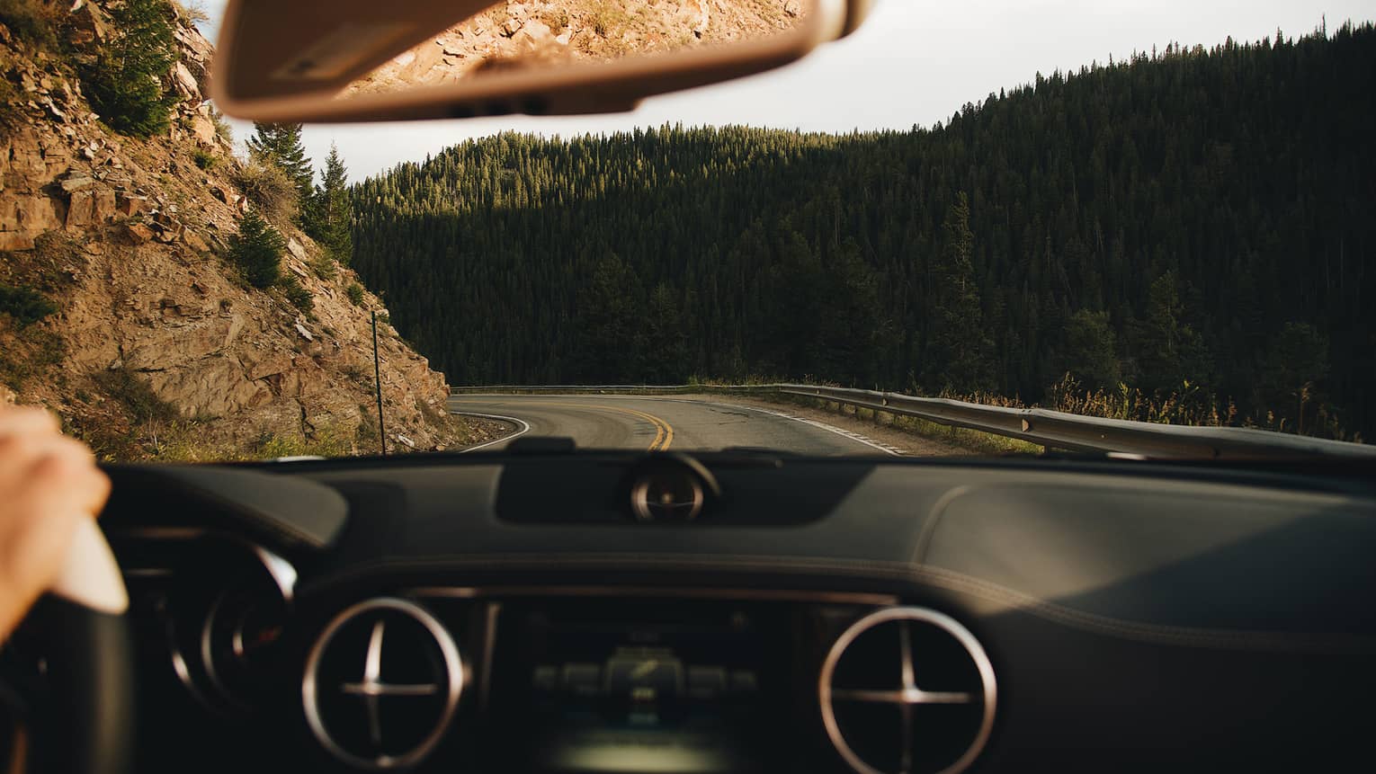 View from behind the wheel of car driving along winding mountain road 