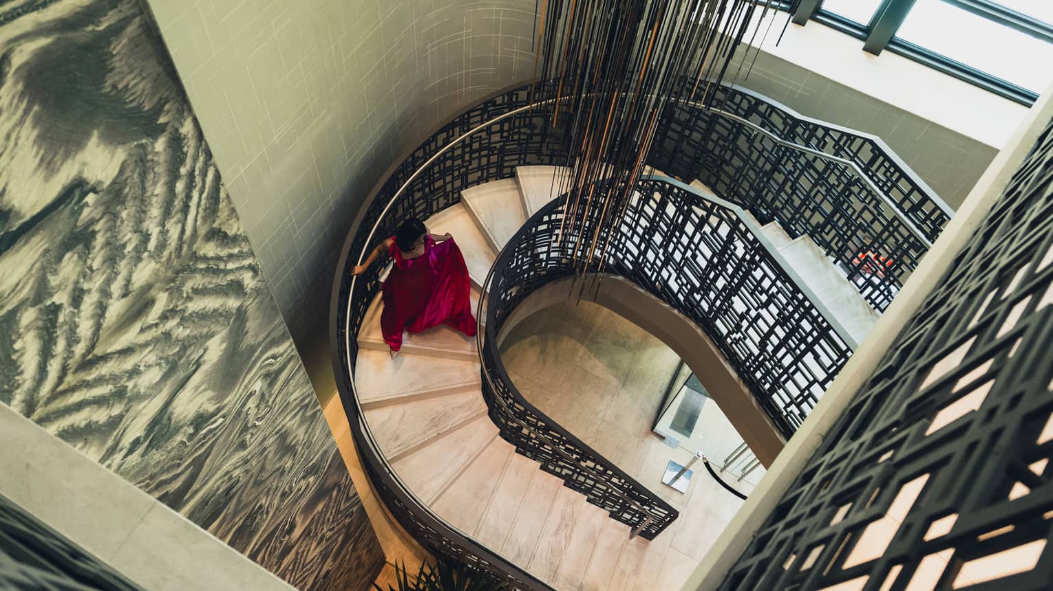 Woman in red evening gown descends a spiral staircase, light streaming in from the window
