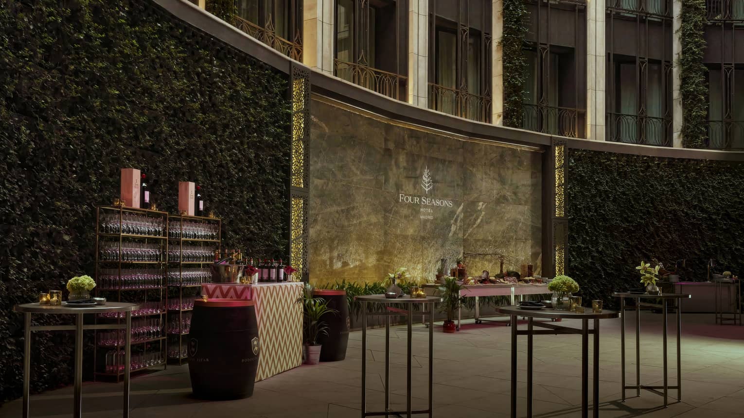 A walled courtyard space with foliage and other plantings, a bar, and several small tables with centerpieces
