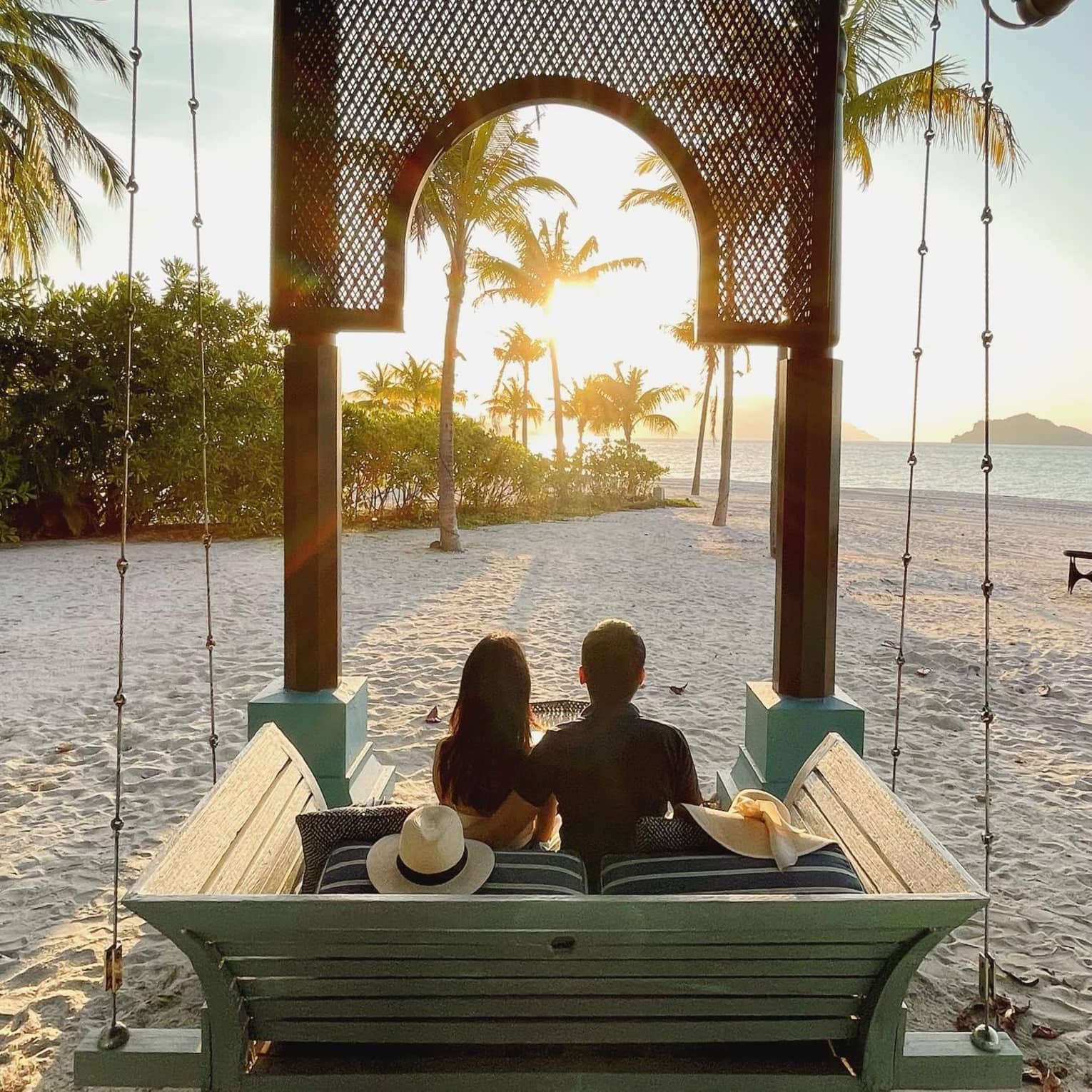 ,A couple watches the sunset from a hanging swing on the beach