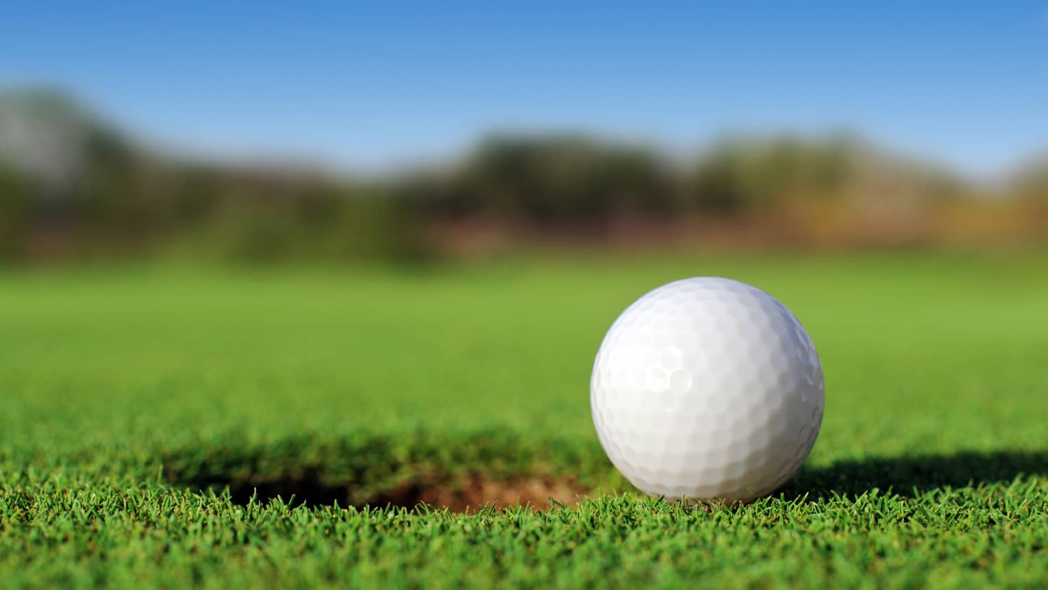A close up of a white golf ball sitting right next to a golf hole on the course