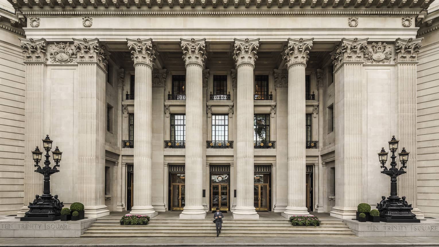 Man in suit and black hat walks down steps under tall white pillars of building