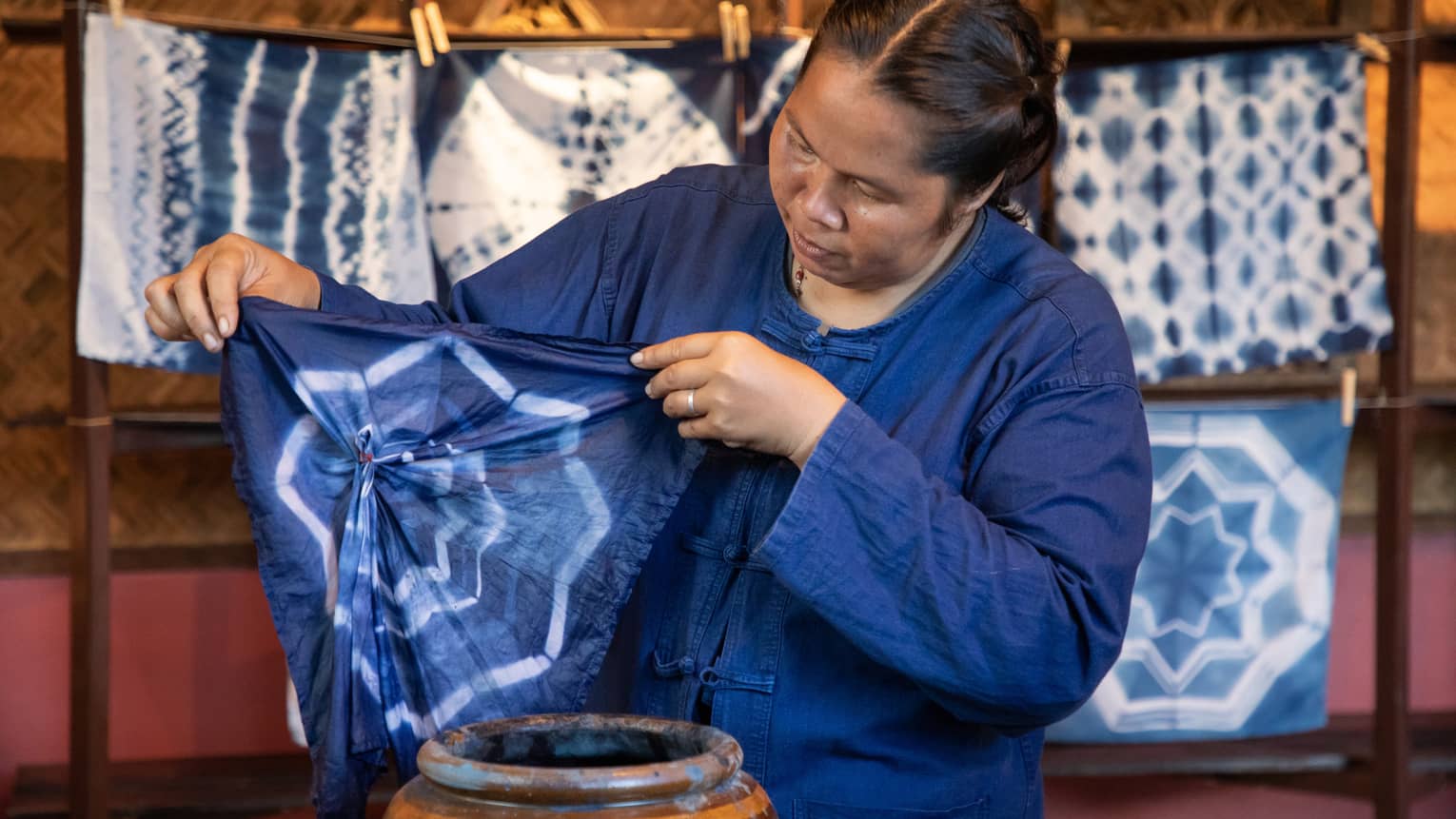 A woman in a blue overshirt, dyeing a piece of fabric.