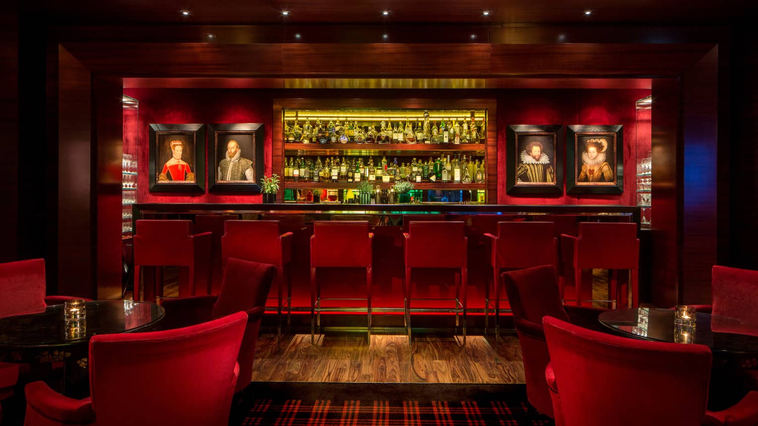 Dimly-lit Amaranto Bar with red accents, lighting, framed oil portraits on each side