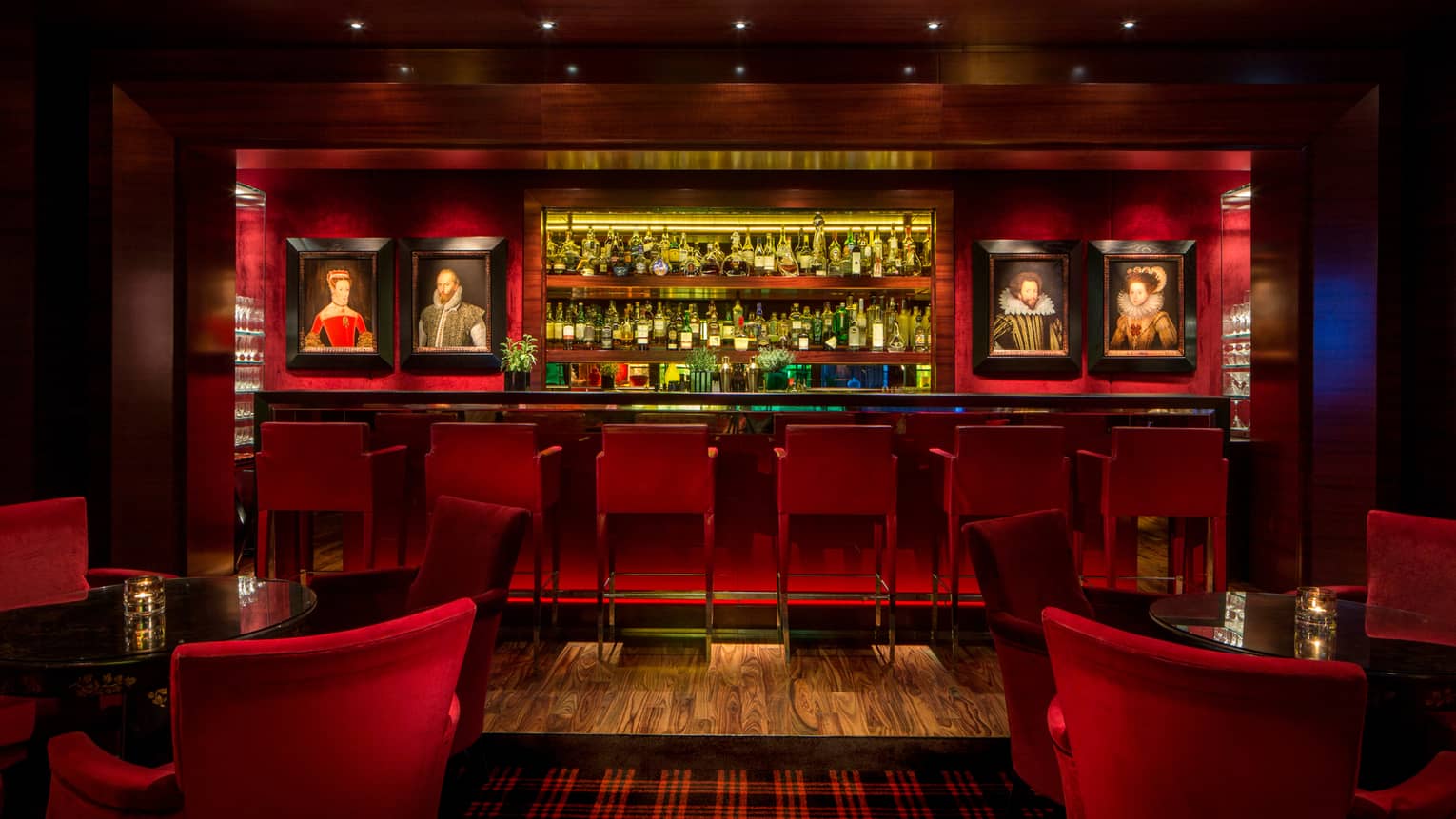 Dimly-lit Amaranto Bar with red accents, lighting, framed oil portraits on each side