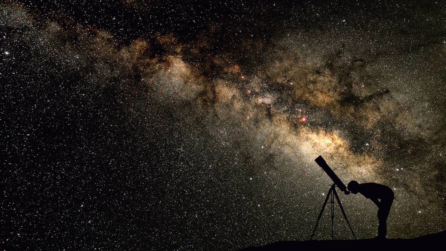 Silhouette of stargazer leaning into telescope against a starry sky, milky way