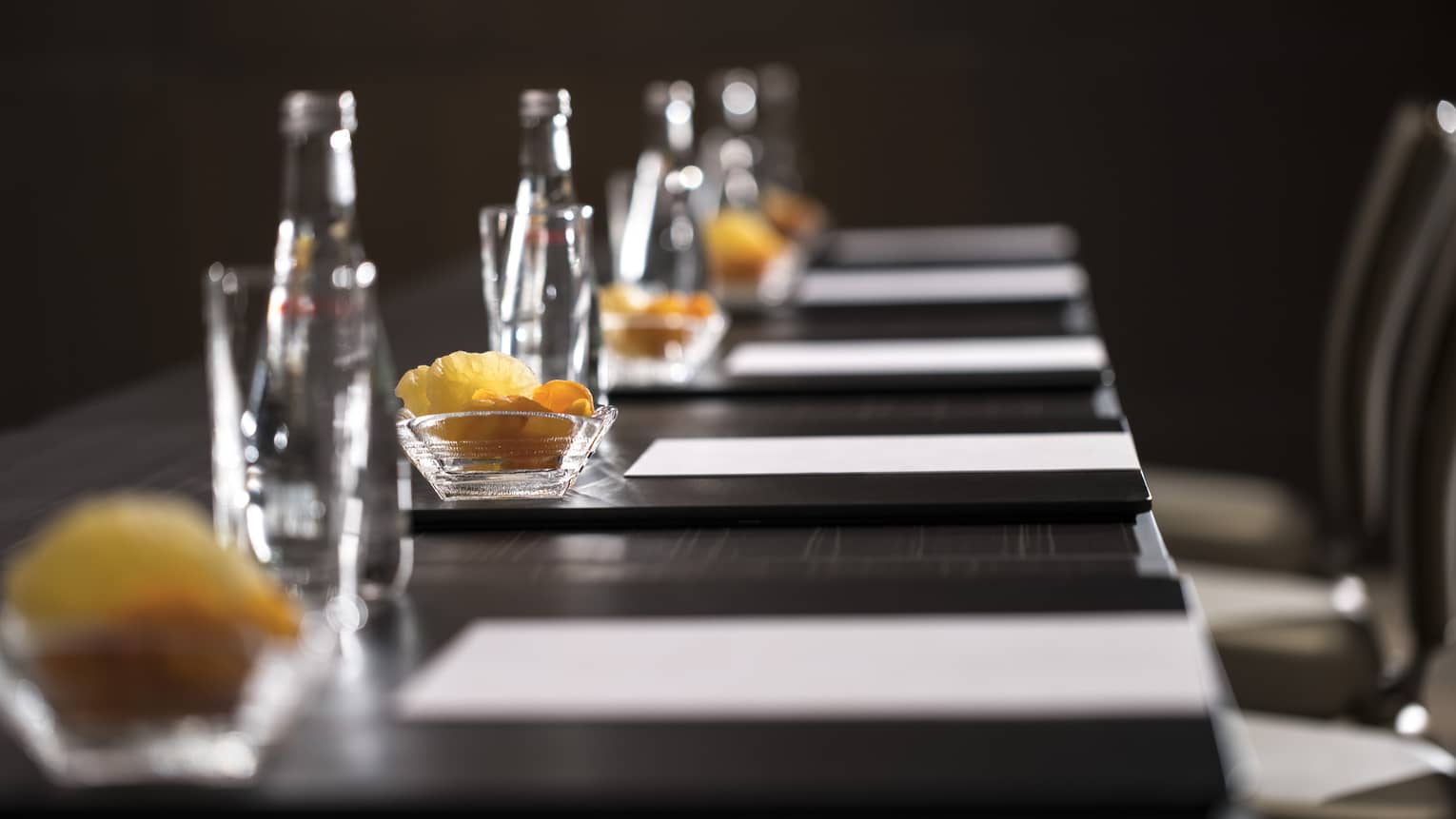 Row of glass bottles, small dishes with dried fruits, meeting agendas along boardroom table