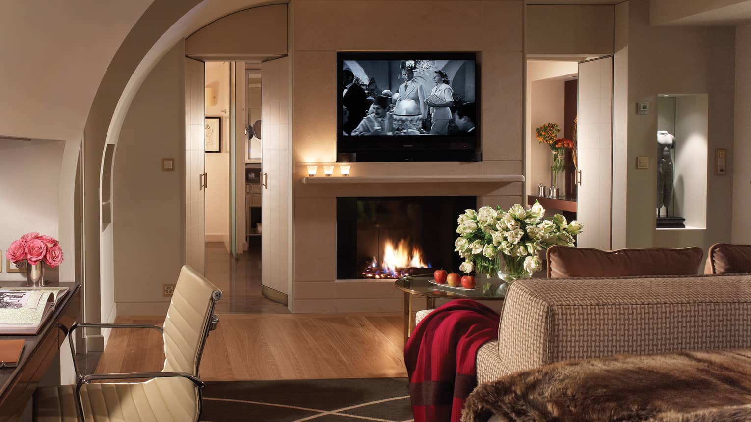 Flat-screen TV showing black-and-white-movie above glass fireplace, sofa with red blanket on arm