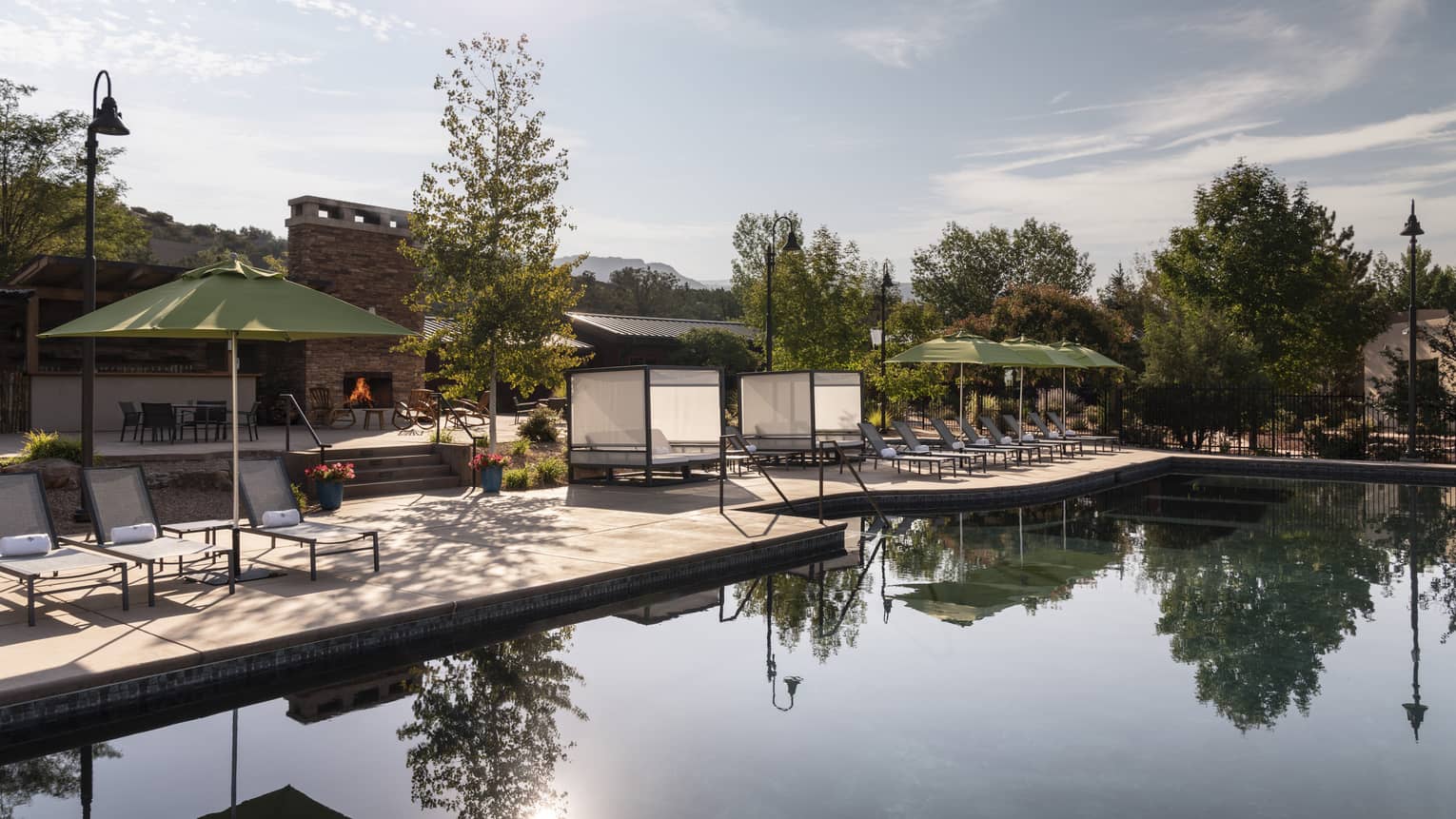 An outdoor pool with lounge chairs and green umbrellas near it.