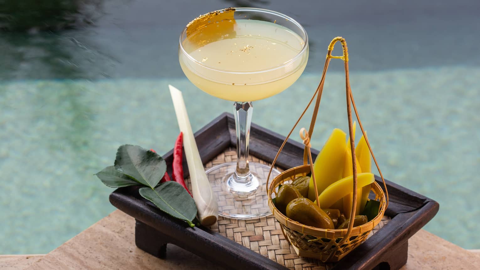 Thai cocktail on poolside tray with lime leaves, lemongrass and chilli garnishes