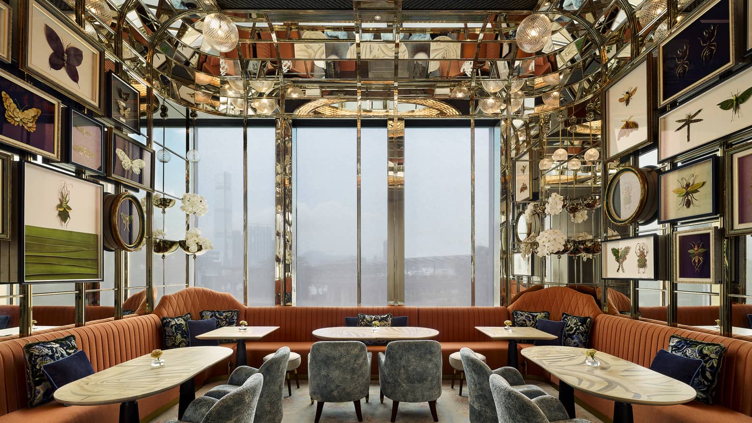 A dining setup with several orange velvet couches, and framed insects on the wall.