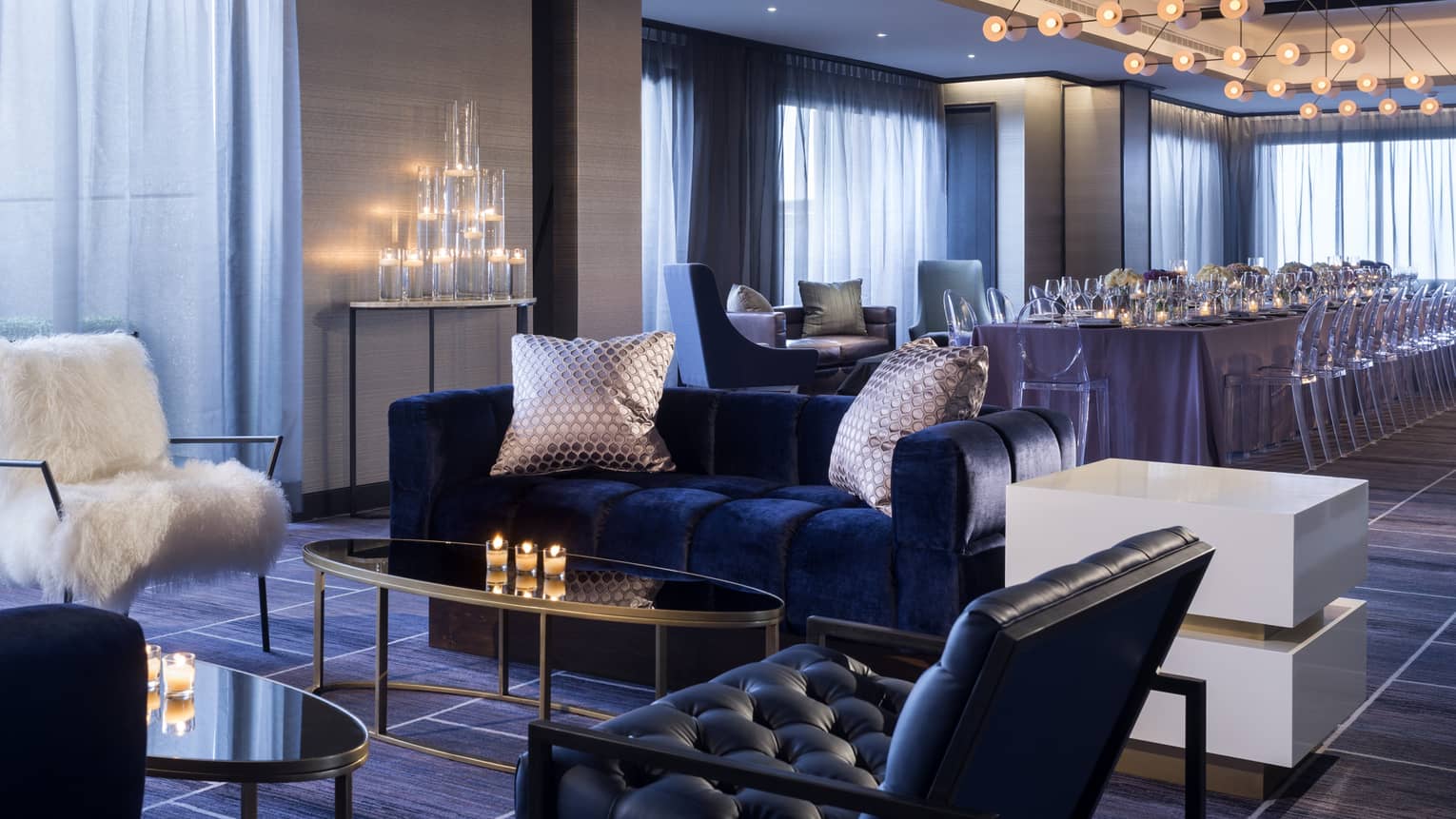 Penthouse seating area with blue velvet sofa, white faux fur chair by candles, long private dining table