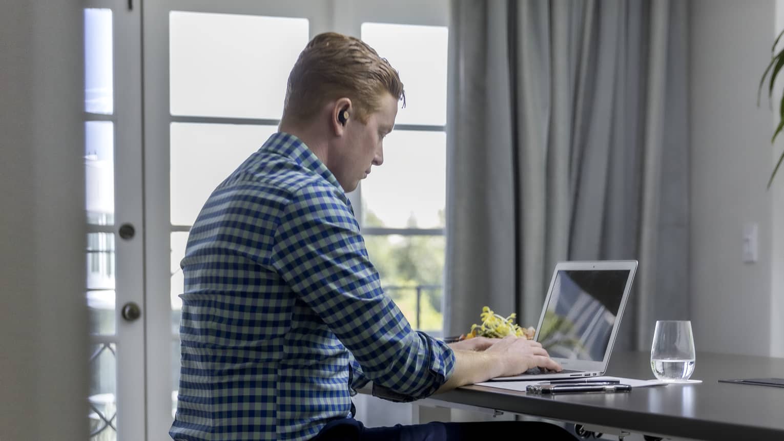 A man in business casual clothing sitting at a desk using a laptop.