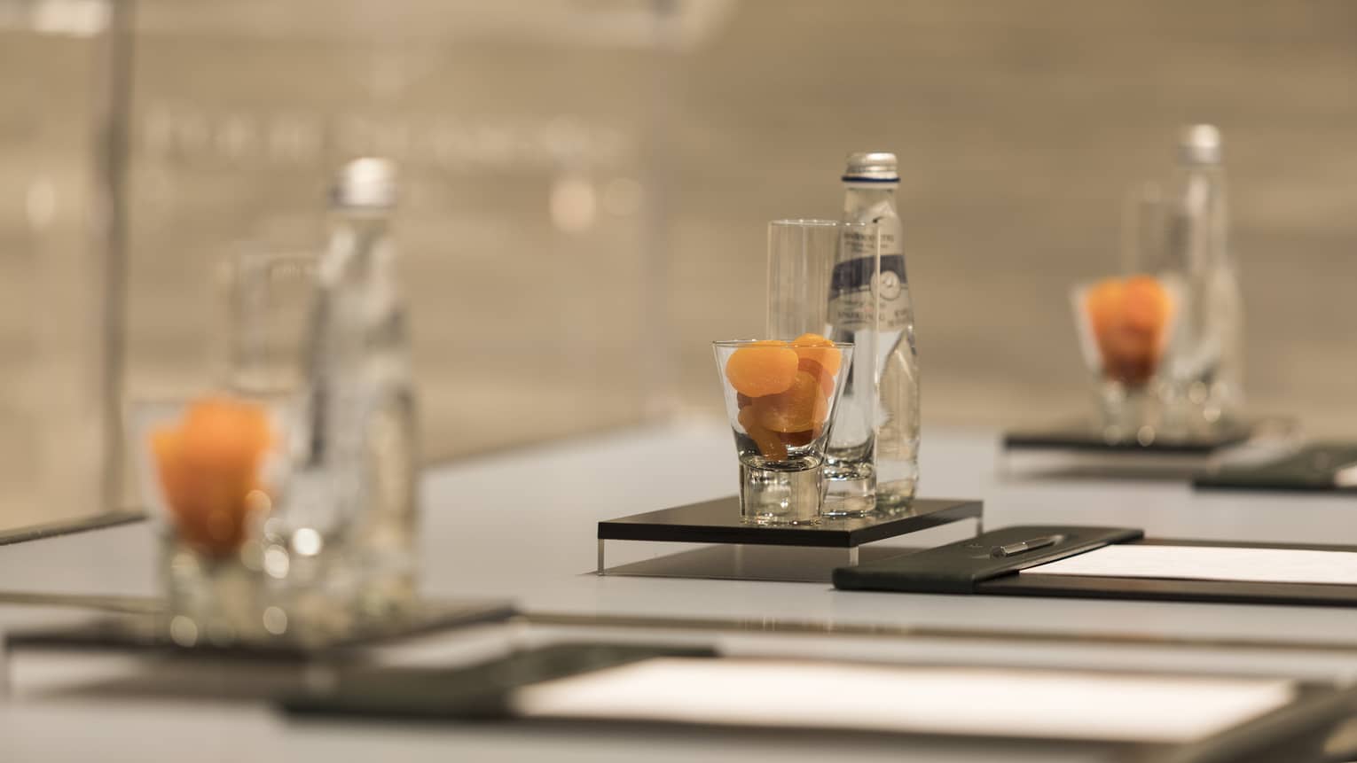 Close-up of meeting table place setting with agenda, dried apricots in glass, bottle of sparkling water