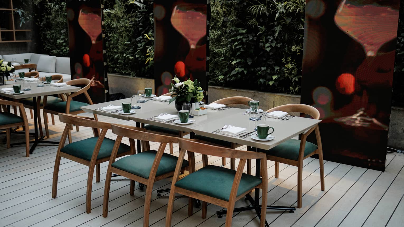 Outdoor terrace with two rectangular tables each set for six, a wall of greenery and three large paper lanters