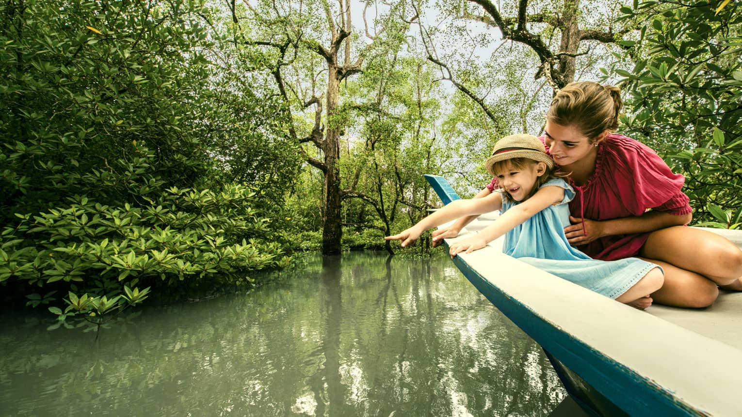 Mom, young daughter in back of wood canoe look into river