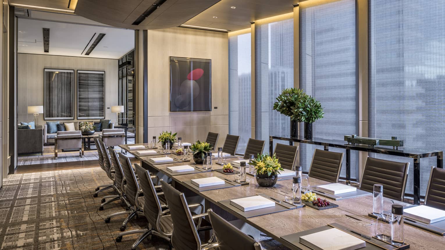 Long board table with flowers, fruit, water, lined with chairs in executive meeting suite
