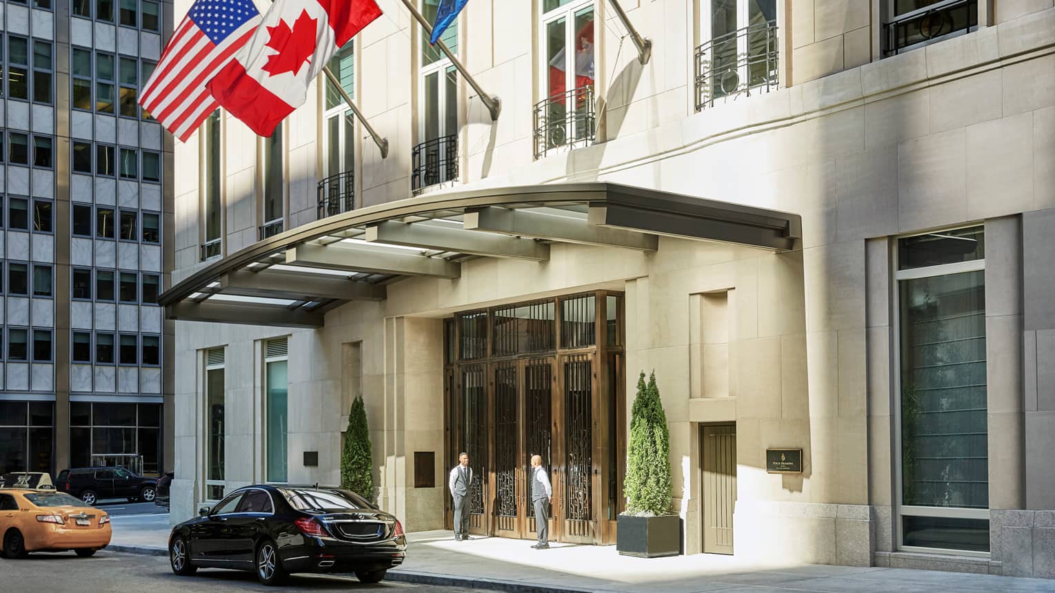 American and Canadian flags fly over Four Seasons Hotel New York Downtown entrance, door staff