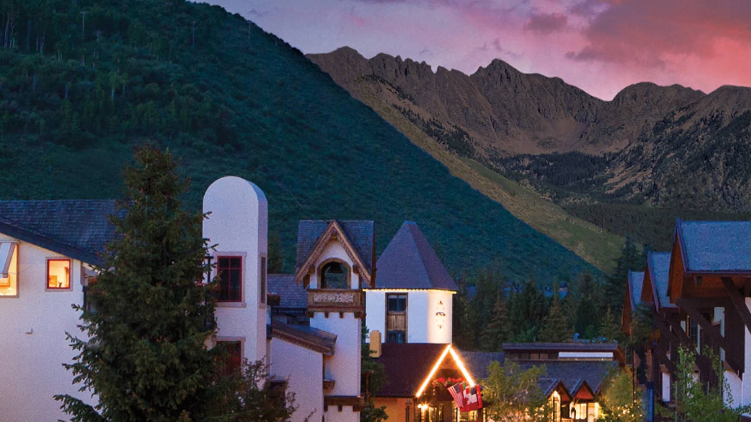 A sunset over a small village like city center with white buildings and mountains in the distance.