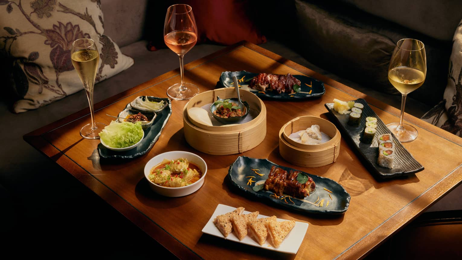 Assorted dim sum and glasses of wine on square wooden table
