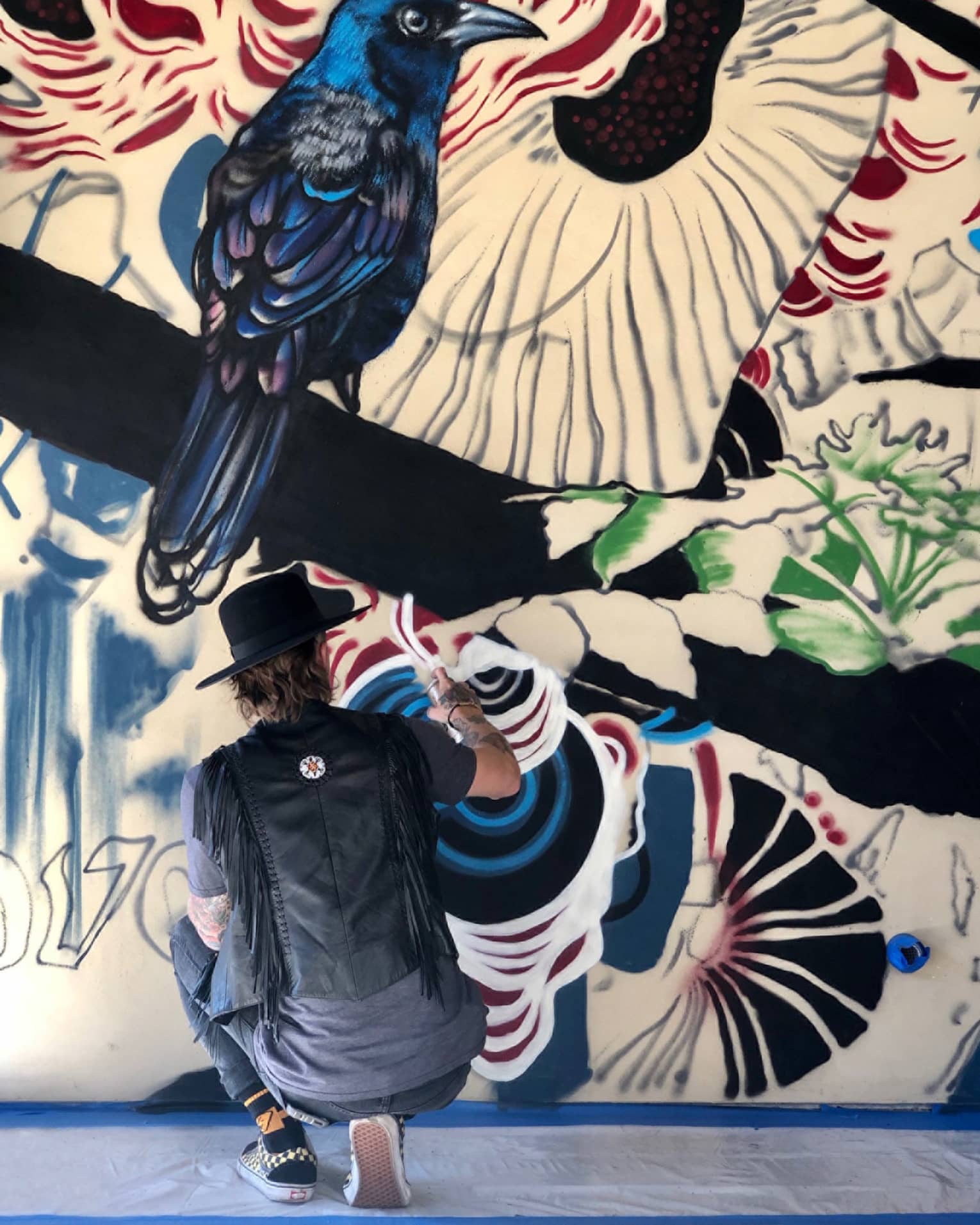Graffiti artist paints a mural featuring a black crow