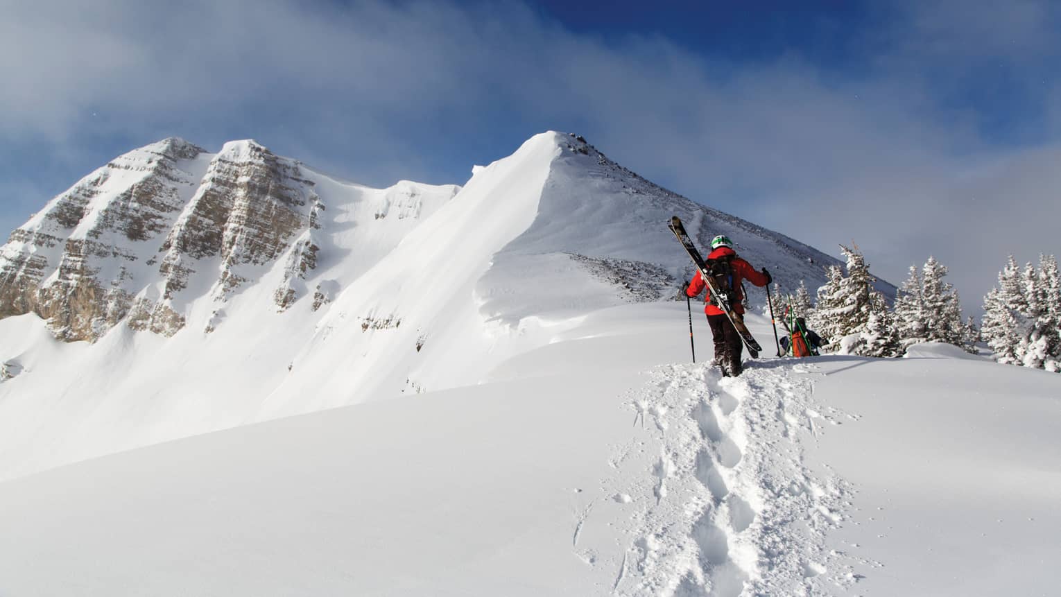 Two people with skis on their backs walking in snow.