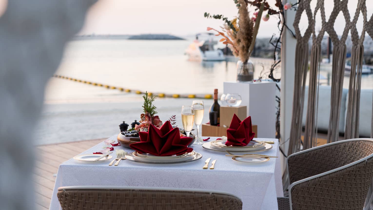 A table set for two with two glasses of champagne on a pier overlooking a calm sea.