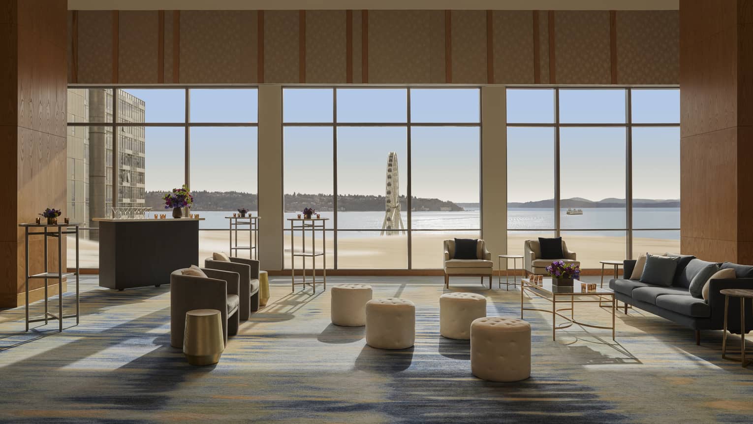 A large room with sofas, chairs, standing tables, stools and large windows.