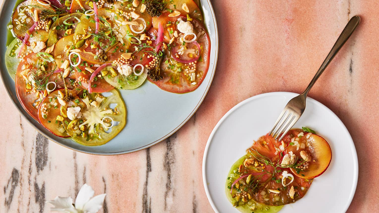 A large and small plate with thinly sliced vegetables and herbs.