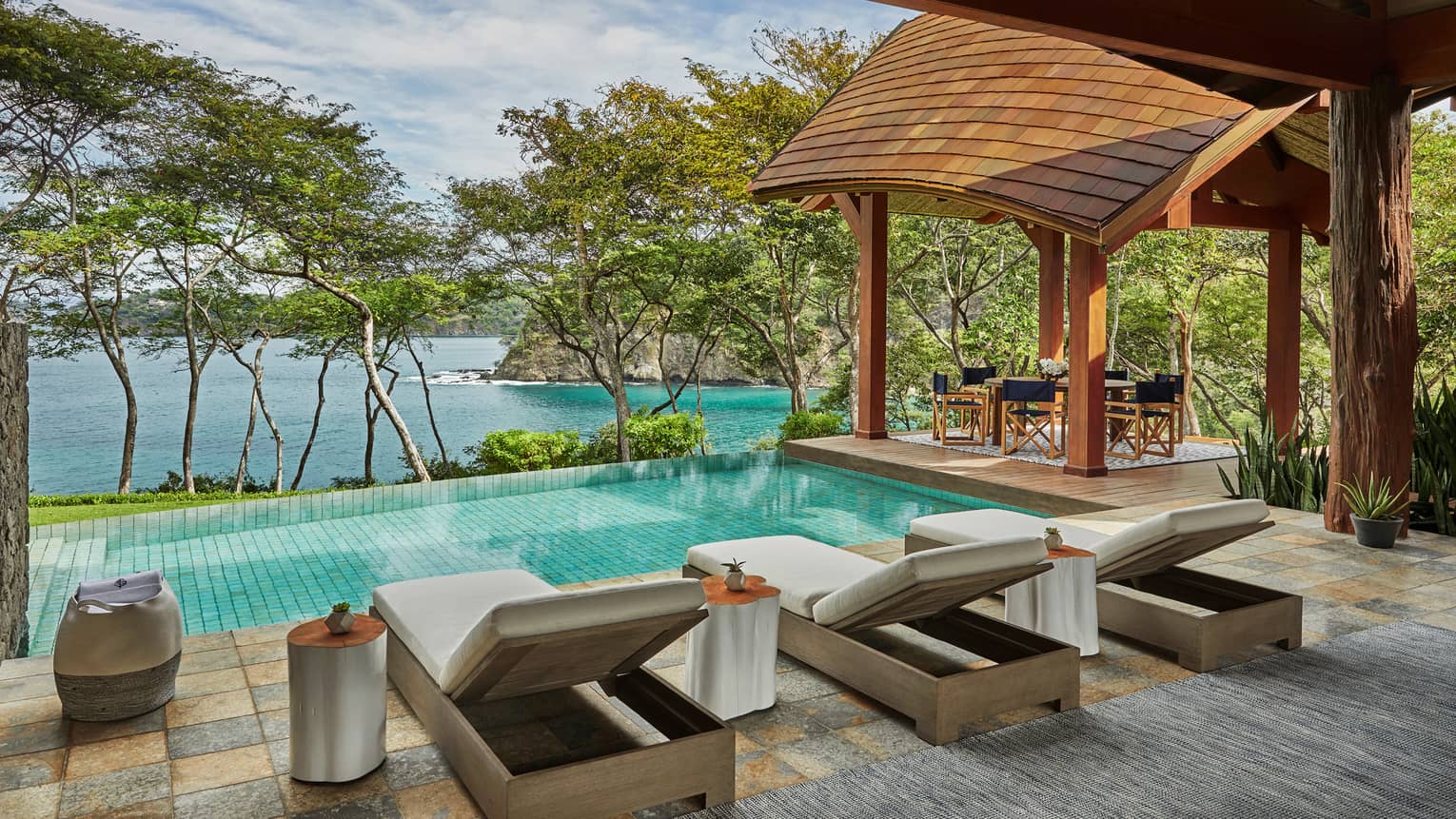 Miramar Suite patio tile patio, three long lounge chairs in front of plunge pool, row of trees, overlooking ocean