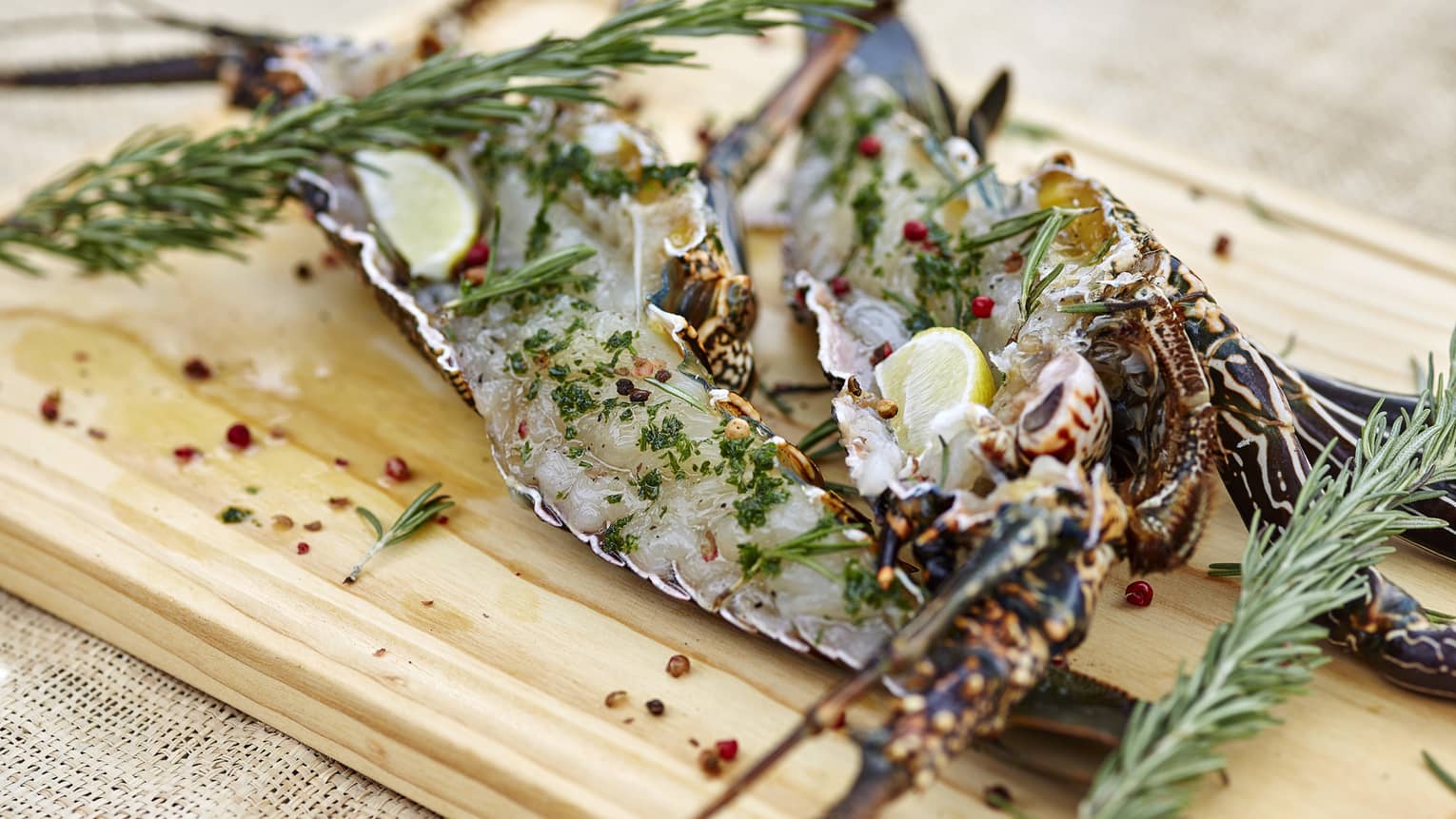 Fresh, raw lobster on a wooden board, with fresh rosemary sprigs and crushed red pepper flakes