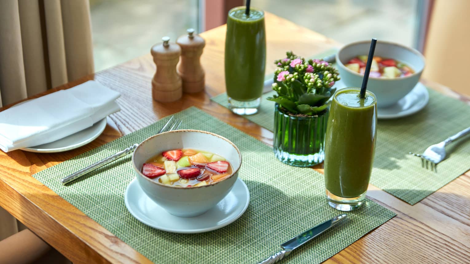 Two place settings on a table, bowls of fruit and green smoothies