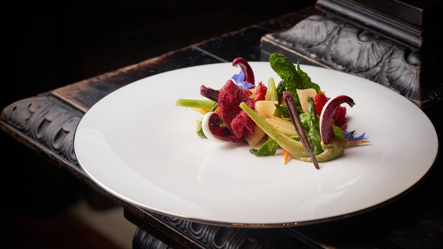 Like an Arcimboldo artwork, seasonal raw and cooked colourful vegetables on white plate
