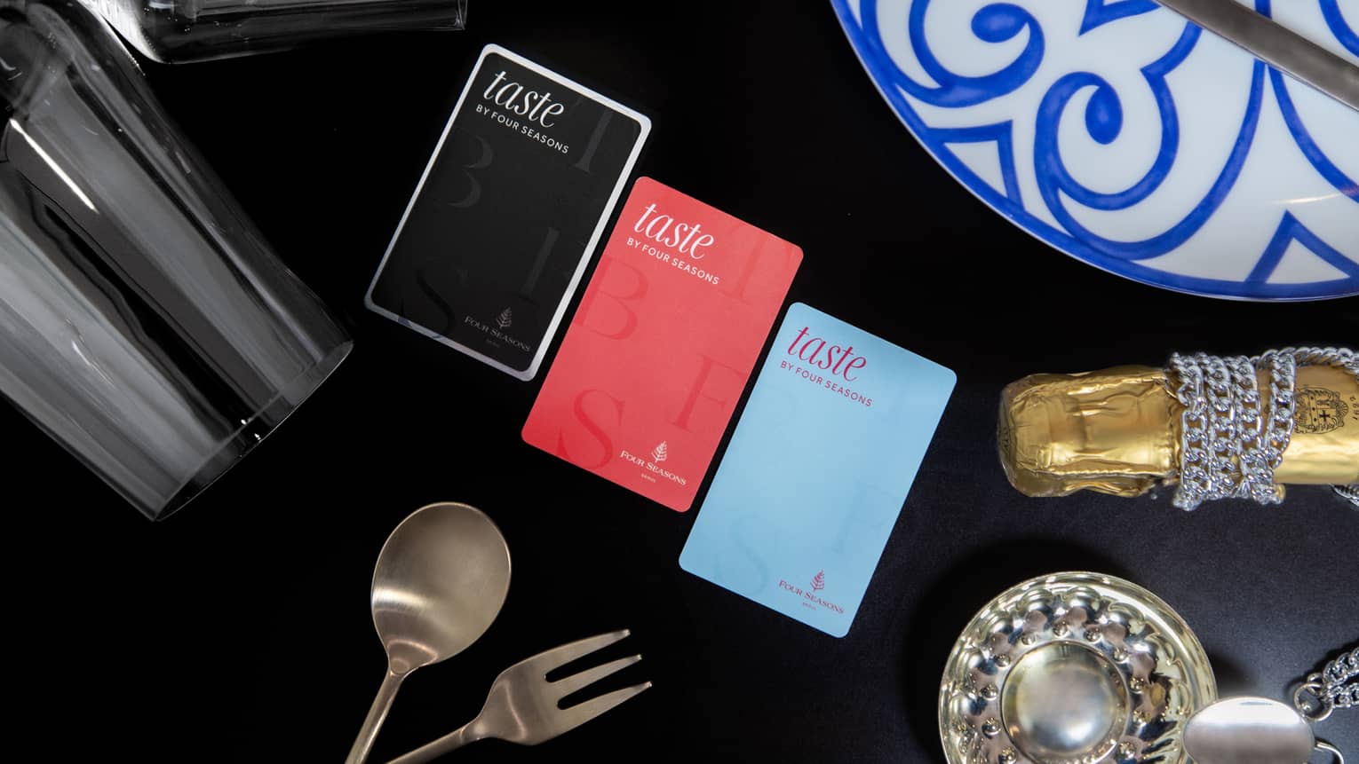 Three colours of Taste by Four Seasons cards on table with black tablecloth, stemmed wine glasses and silver cutlery