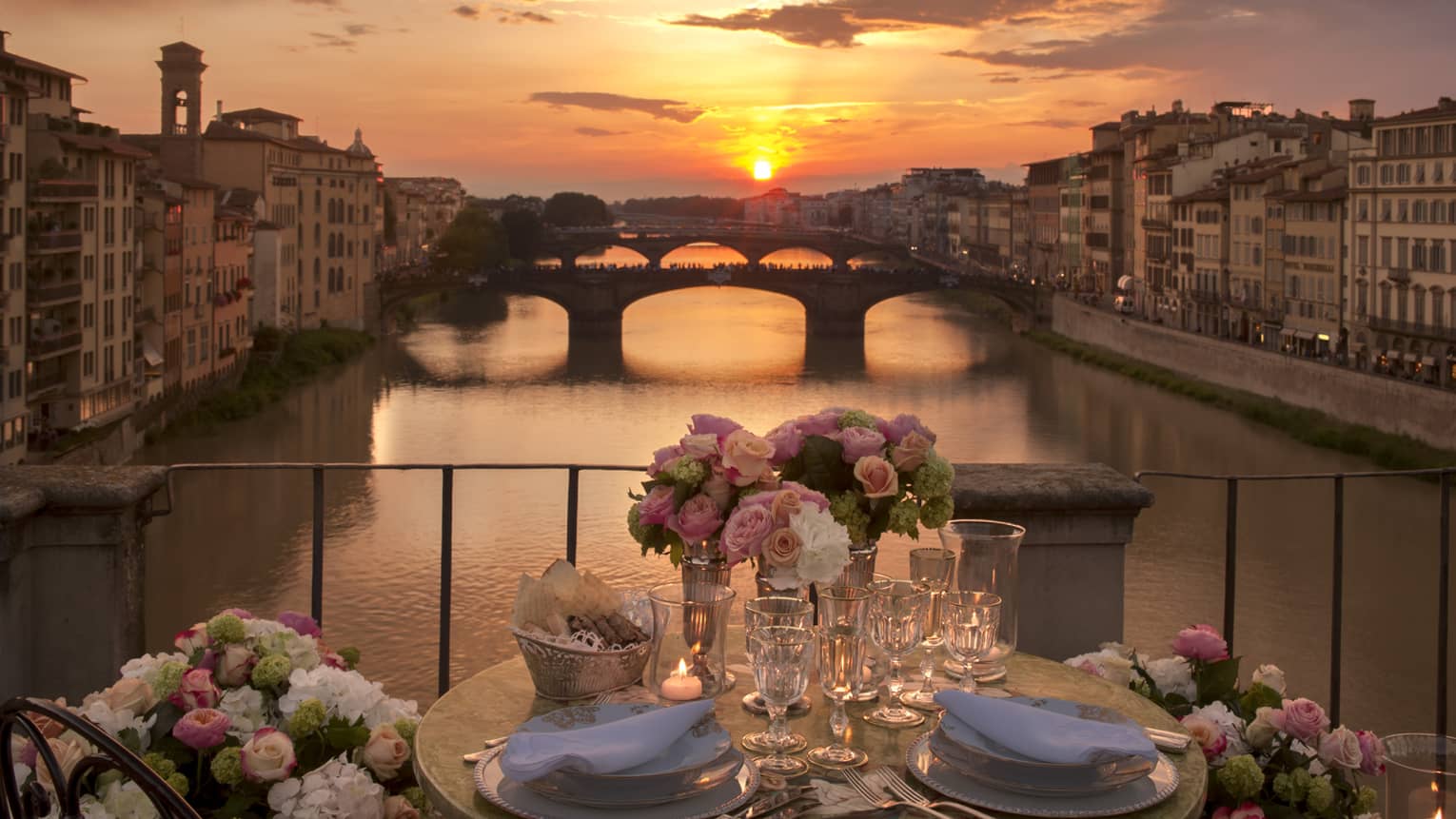 Pink roses in vases on formal dining table on bridge overlooking canal, sunset