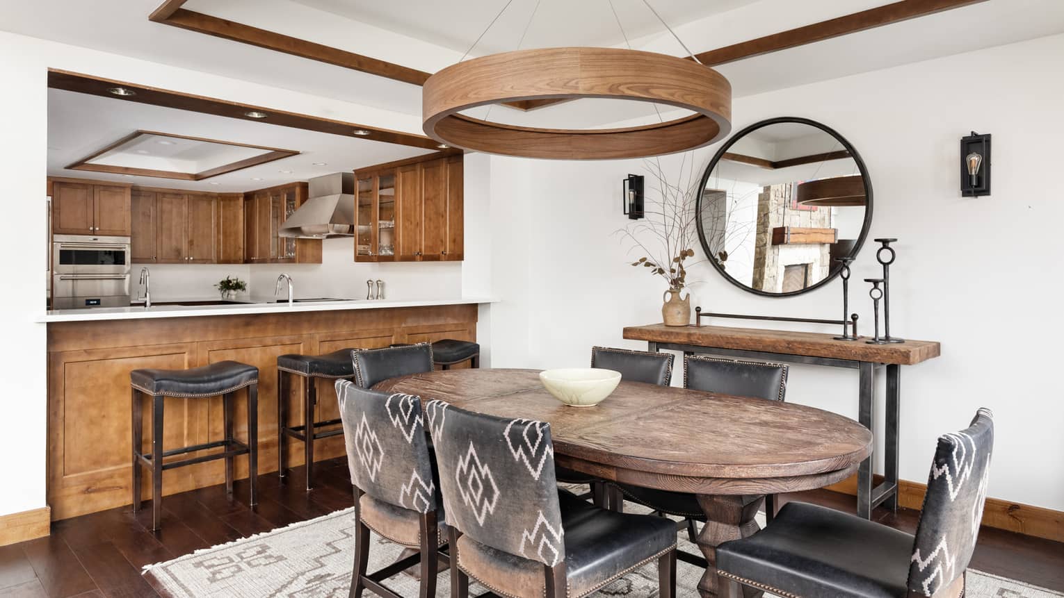 Mountain chic dining room with a rustic touch, featuring a wooden table, six leather chairs and open view to a kitchen with wood cabinetry